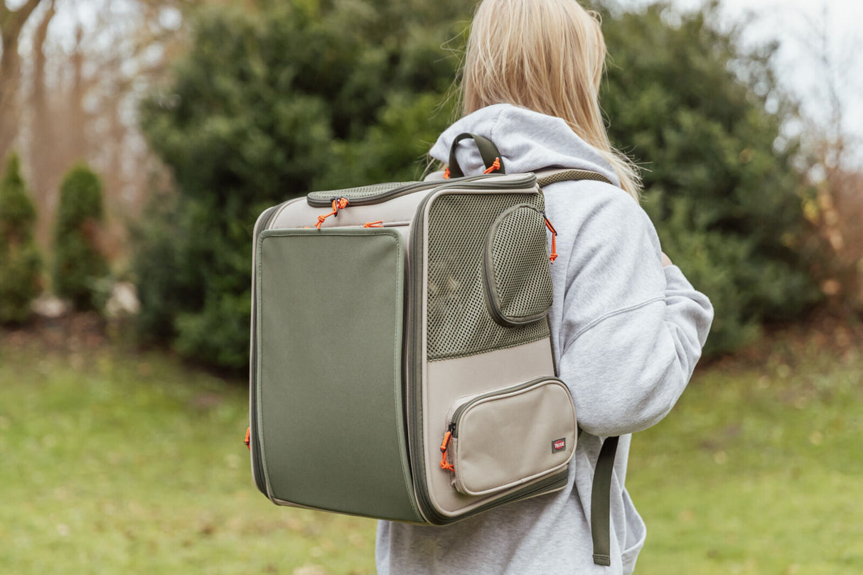 Person trägt einen olivgrünen Transportrucksack mit orangefarbenen Details im Freien.