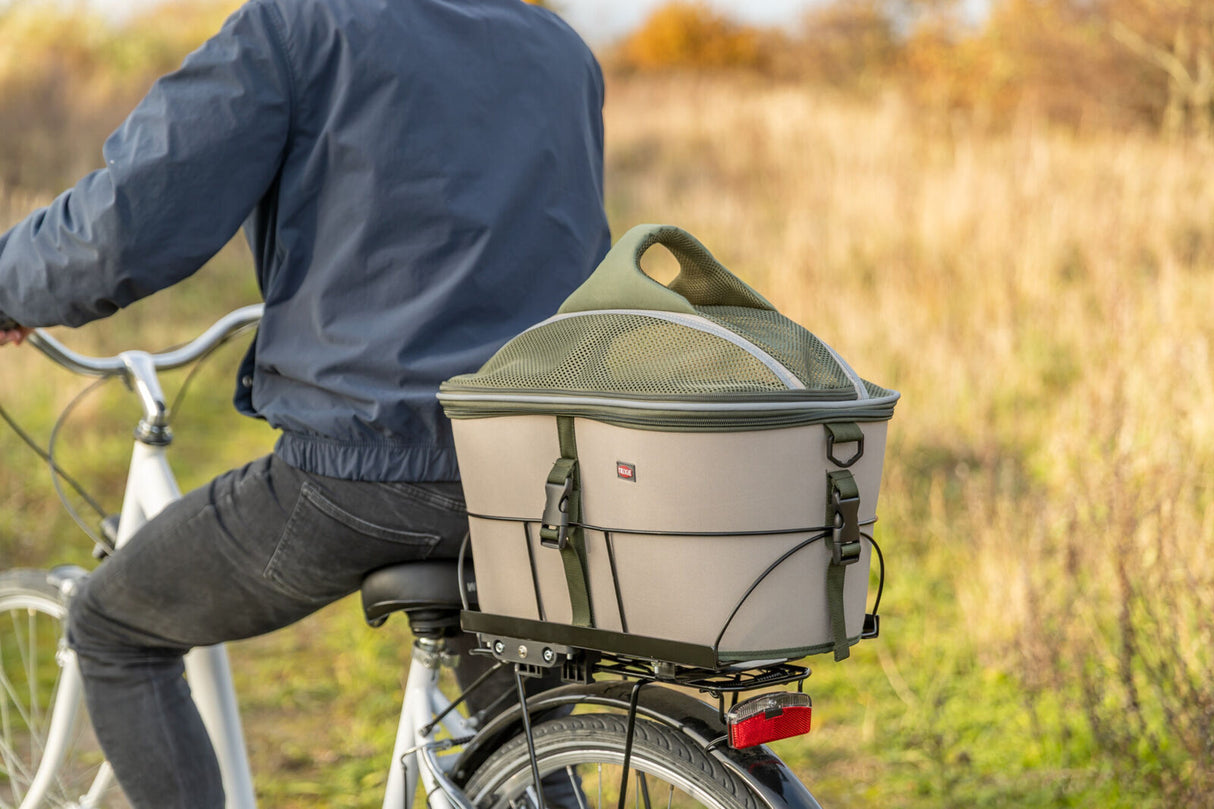 Transportbox auf einem Fahrradgepäckträger, Fahrer mit blauer Jacke, Hintergrund Wiese.