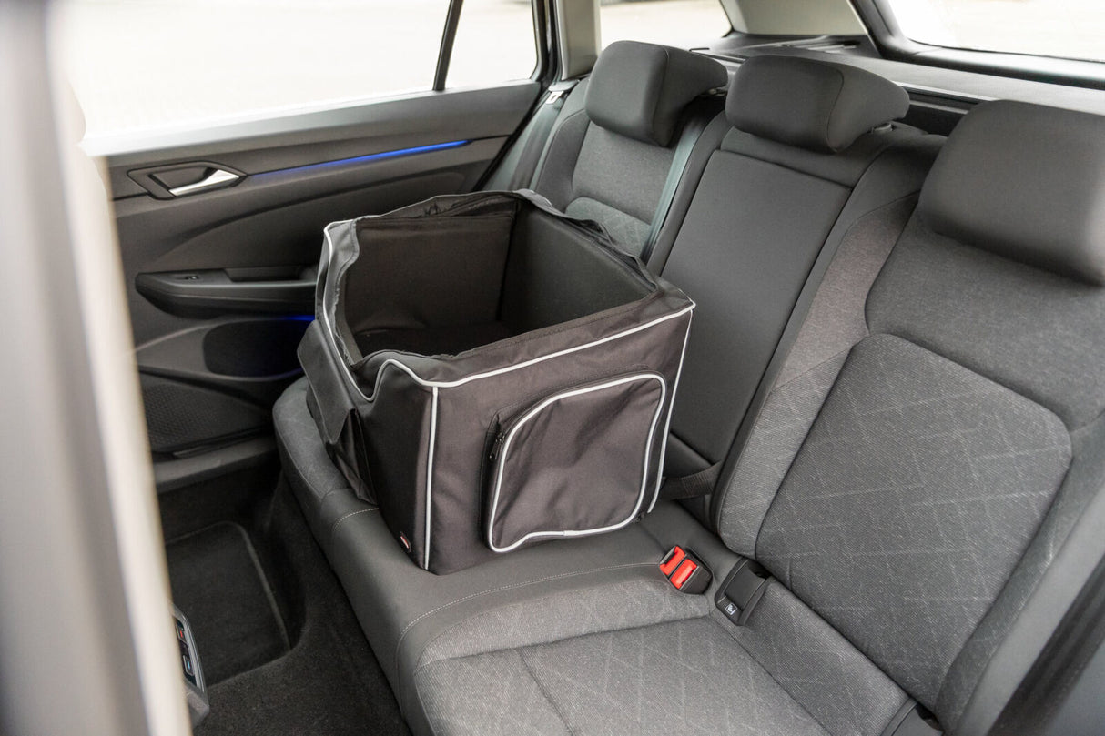 Schwarze Tasche mit weißen Nähten steht auf dem Rücksitz eines Autos, mit grauem Innenraum und blauen Akzenten.