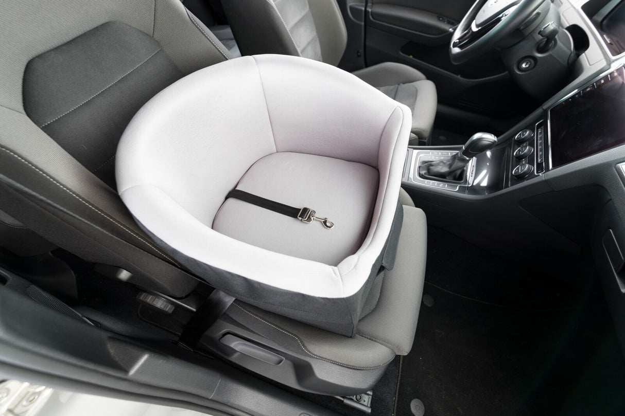 Autositz mit hellgrauer Babyschale und Sicherheitsgurt auf einem schwarzen Sitz im Fahrzeug.