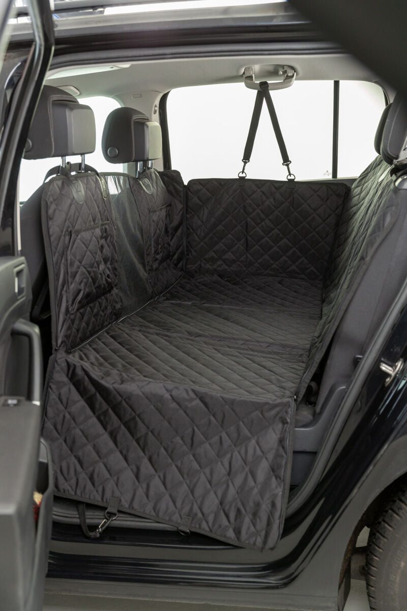 Schwarze, gesteppte Autoschondecke bedeckt die Rückbank und Innenraum eines Autos, Kopfstützen und Sicherheitsgurte sichtbar.