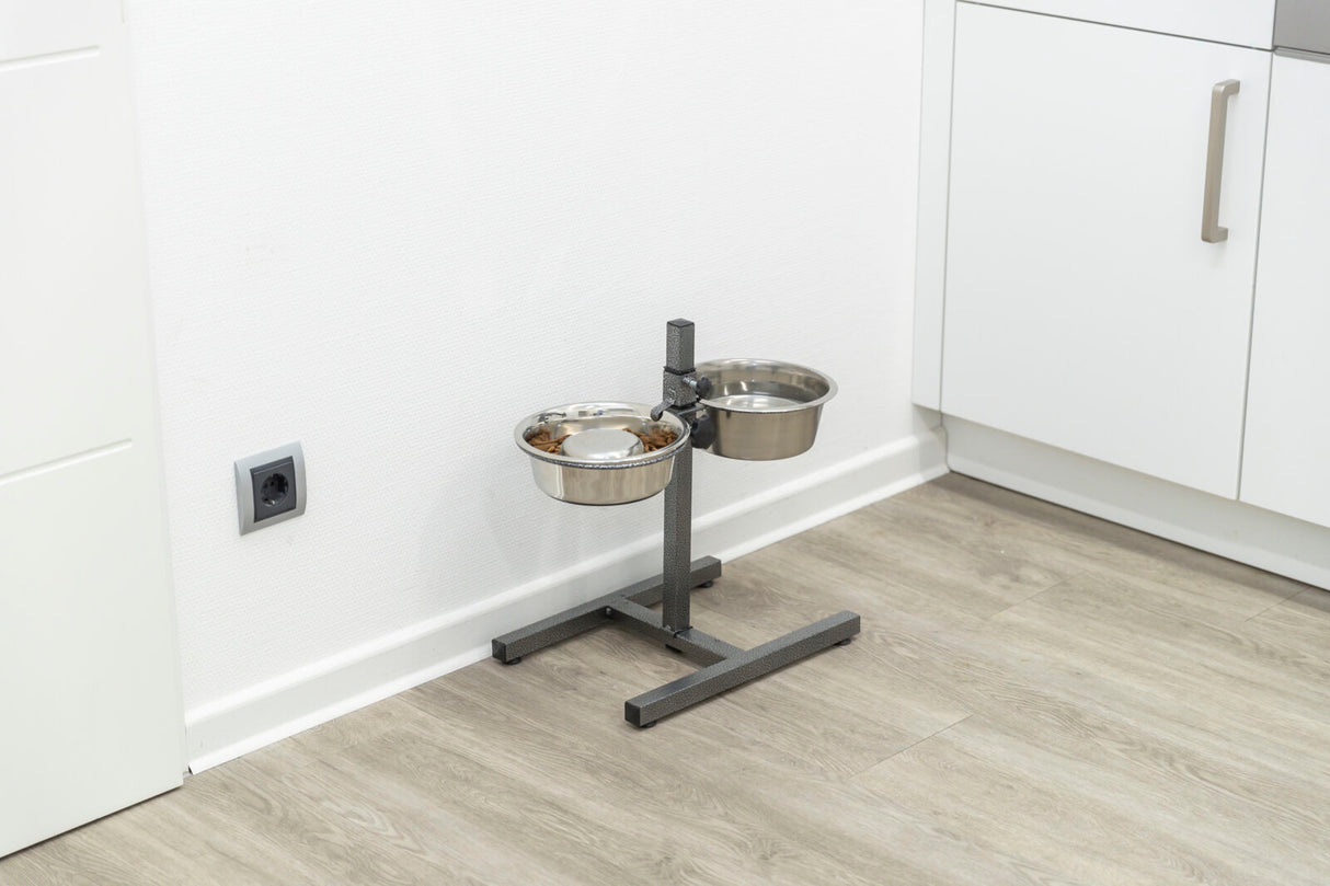 Metallständer mit zwei Edelstahl-Napfhaltern, einer enthält Futter, auf hellem Holzboden vor weißer Wand.