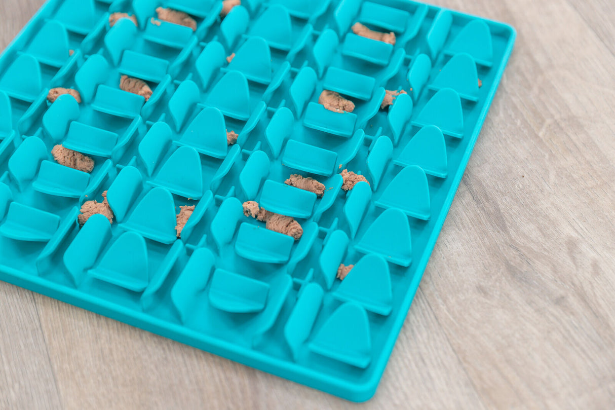 Blaue Matte mit erhabenen Formen und verstreuten kleinen Portionen brauner Masse auf Holzoberfläche.