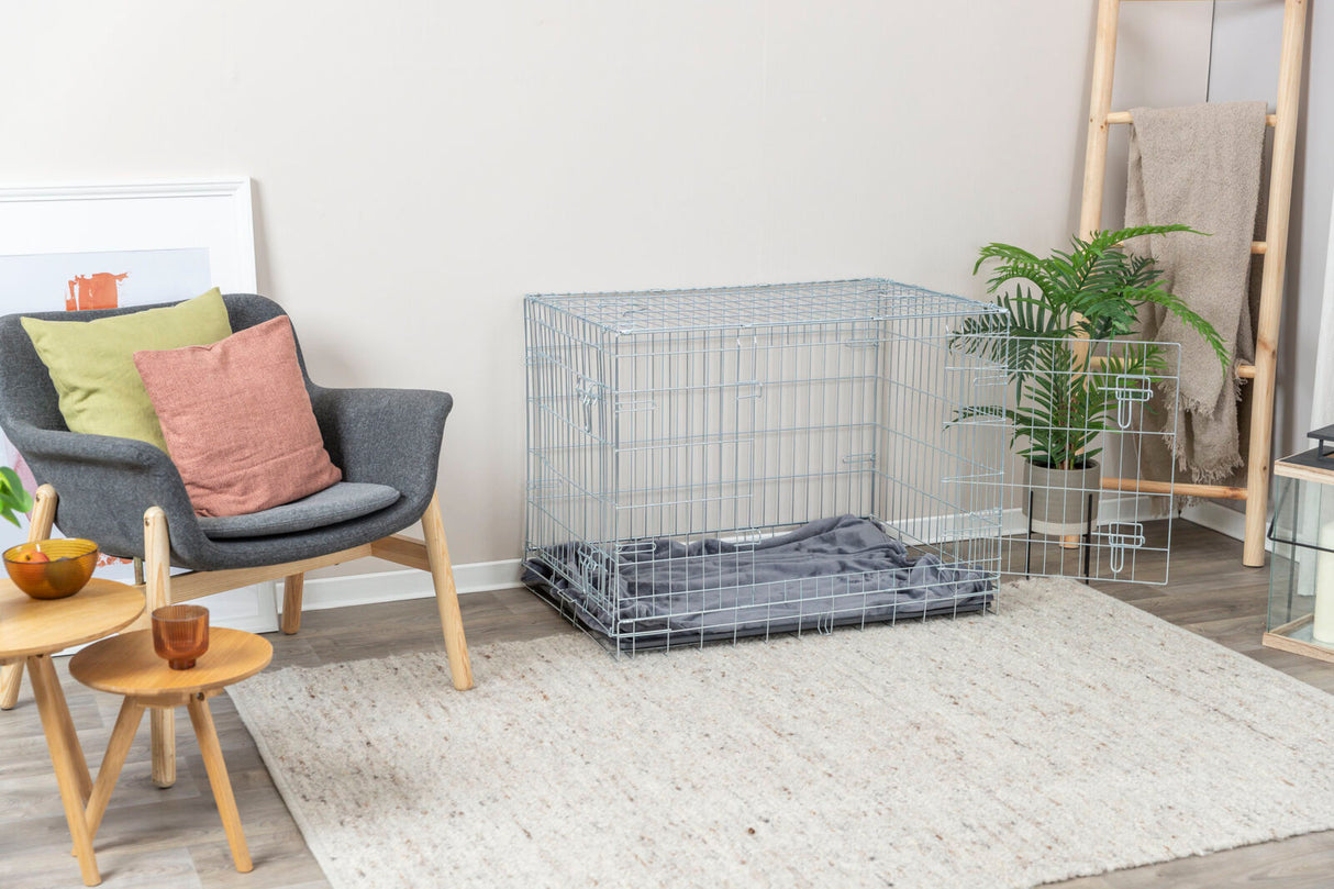 Grau gestreifter Teppich vor einem dunklen Sessel mit Kissen, daneben ein Metallkäfig und eine Pflanze.