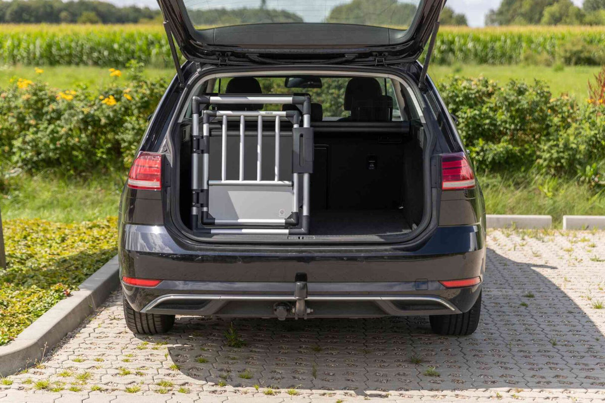 Offener Kofferraum eines Autos mit einem grauen Gitter, im Hintergrund sind grüne Büsche und Bäume sichtbar.