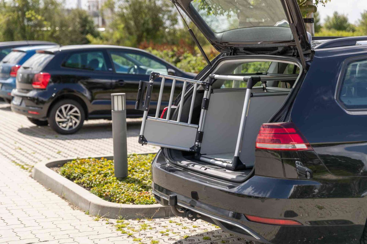 Offener Kofferraum eines schwarzen Autos mit eingebautem weiß-grauem Gitter- und Trägergestell, geparkte Autos im Hintergrund.