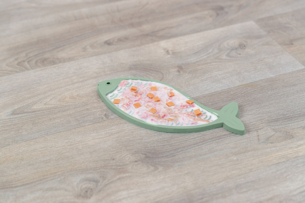 Fischförmige, grüne Unterlage mit bunten Stücken oberhalb auf einem Holzfußboden.