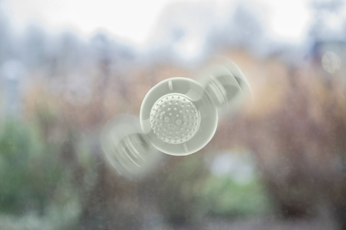 Ein weißes, rundes Spielzeug mit Noppen dreht sich schnell vor einem unscharfen, natürlichen Hintergrund.