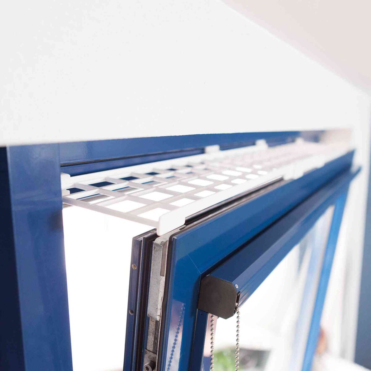 Ein geöffnetes blaues Fenster mit einem weißen Sicherheitsgitter an der Oberseite und einer Kette an der Seite.