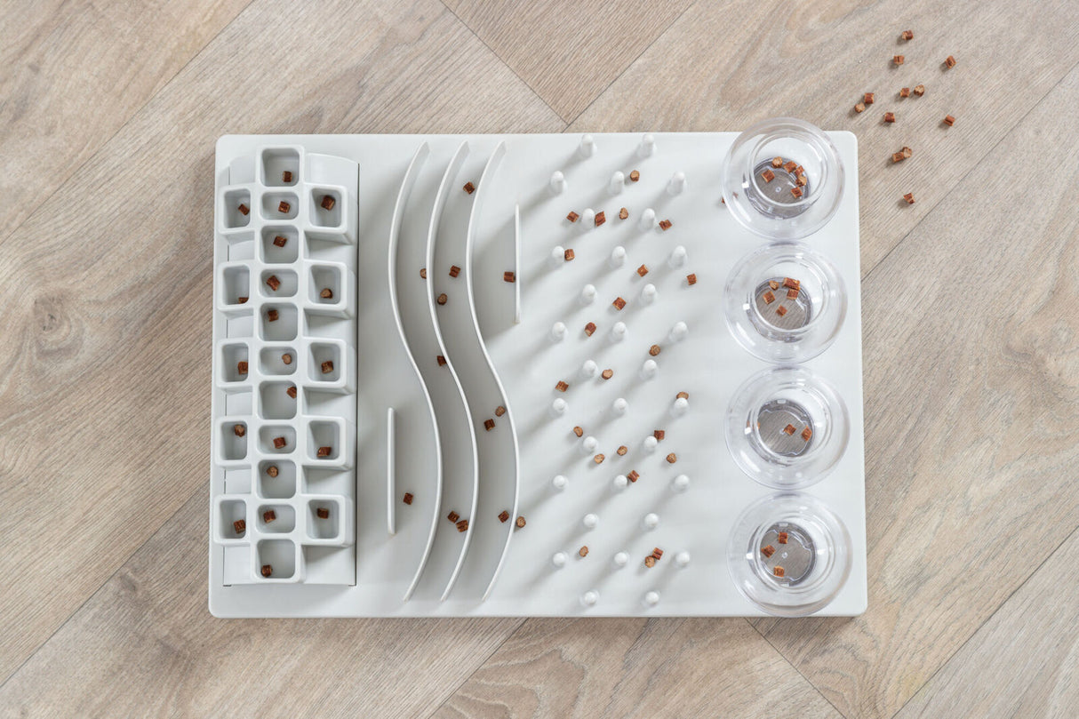 Rechteckige weiße Interaktiv-Matte mit variablen Vertiefungen und Kammern, gefüllt mit kleinen braunen Stücken.