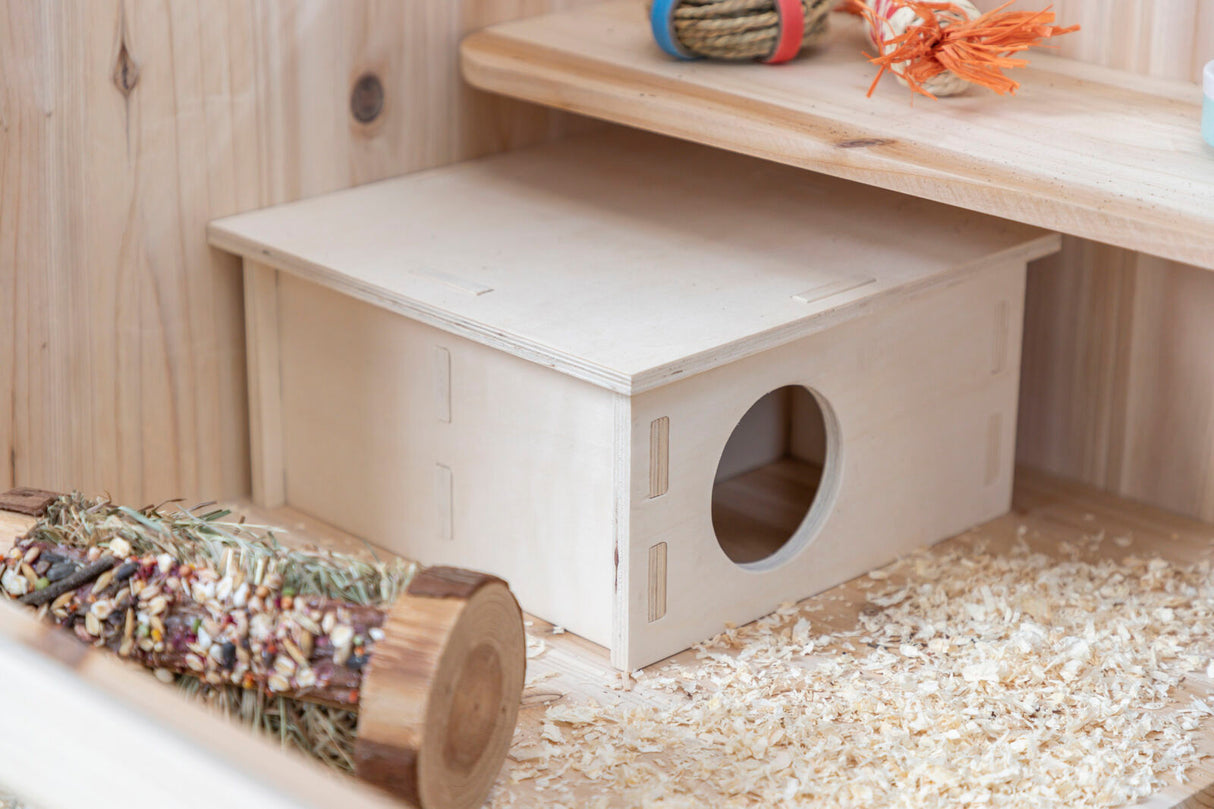 Holzhaus mit rundem Eingang und Sägespänen auf Holzboden, daneben Holzspielzeug und bunte Seile.