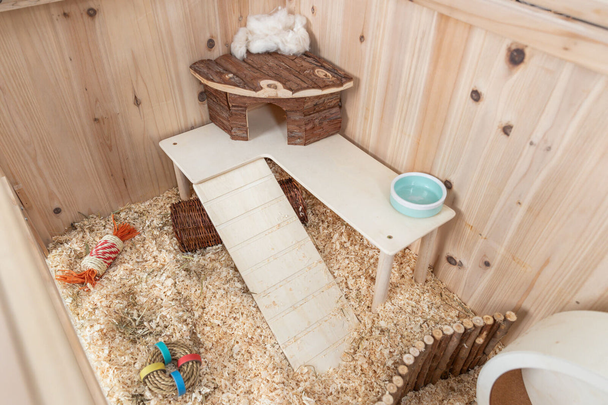 Kleines Gehege mit Holzspänen, Rampe, Häuschen, Wassernapf und Spielzeugen aus Seil und Holz.