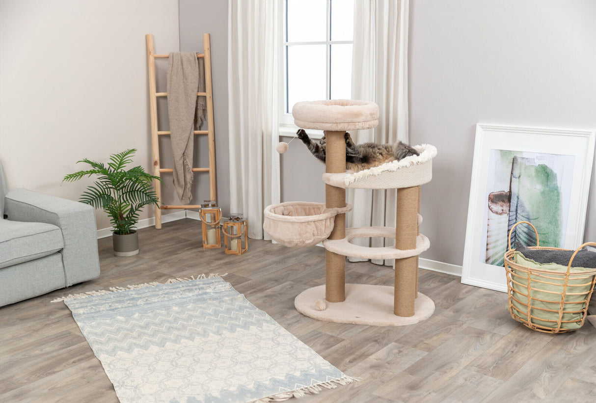 Helles Wohnzimmer mit einem beigen Kratzbaum, auf dem eine Katze liegt, daneben ein Teppich und Pflanzen.