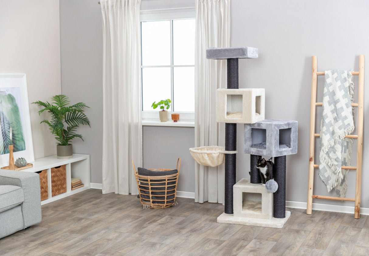 Katzenbaum mit grauen und beigen Elementen steht in einem Wohnzimmer mit Holzboden und Vorhängen, Katze klettert.