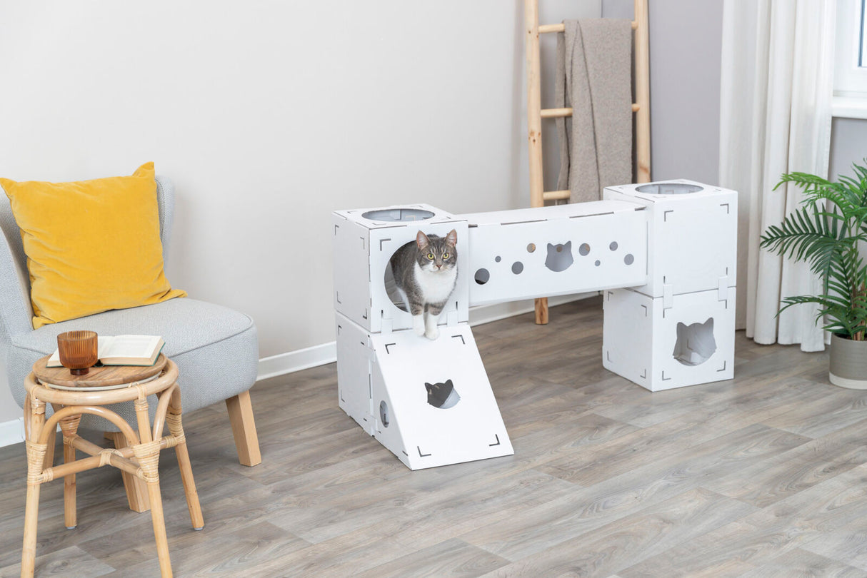 Ein graues, weißes Katzenmöbelstück mit mehreren Ebenen, ein Kissen auf einem Sessel und ein kleiner Tisch.