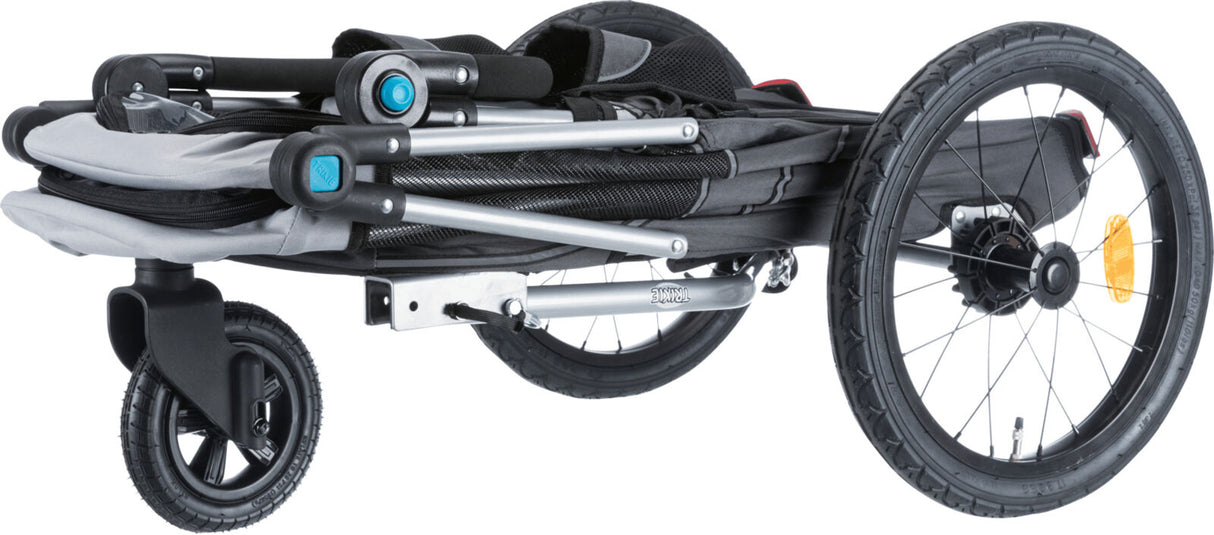 Gefalteter Fahrradanhänger mit schwarzem und grauem Gestell, drei Rädern und sichtbarem Reflektor.