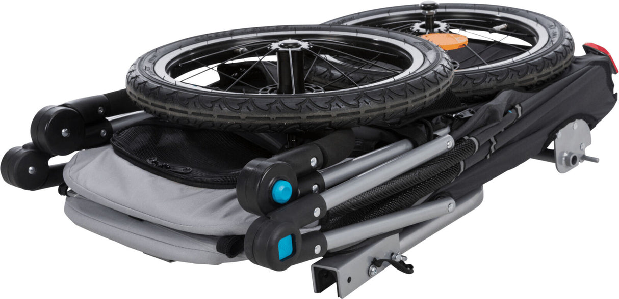 Zusammengeklappter Fahrradanhänger mit schwarzen Rädern und grauem Rahmen auf weißem Hintergrund.