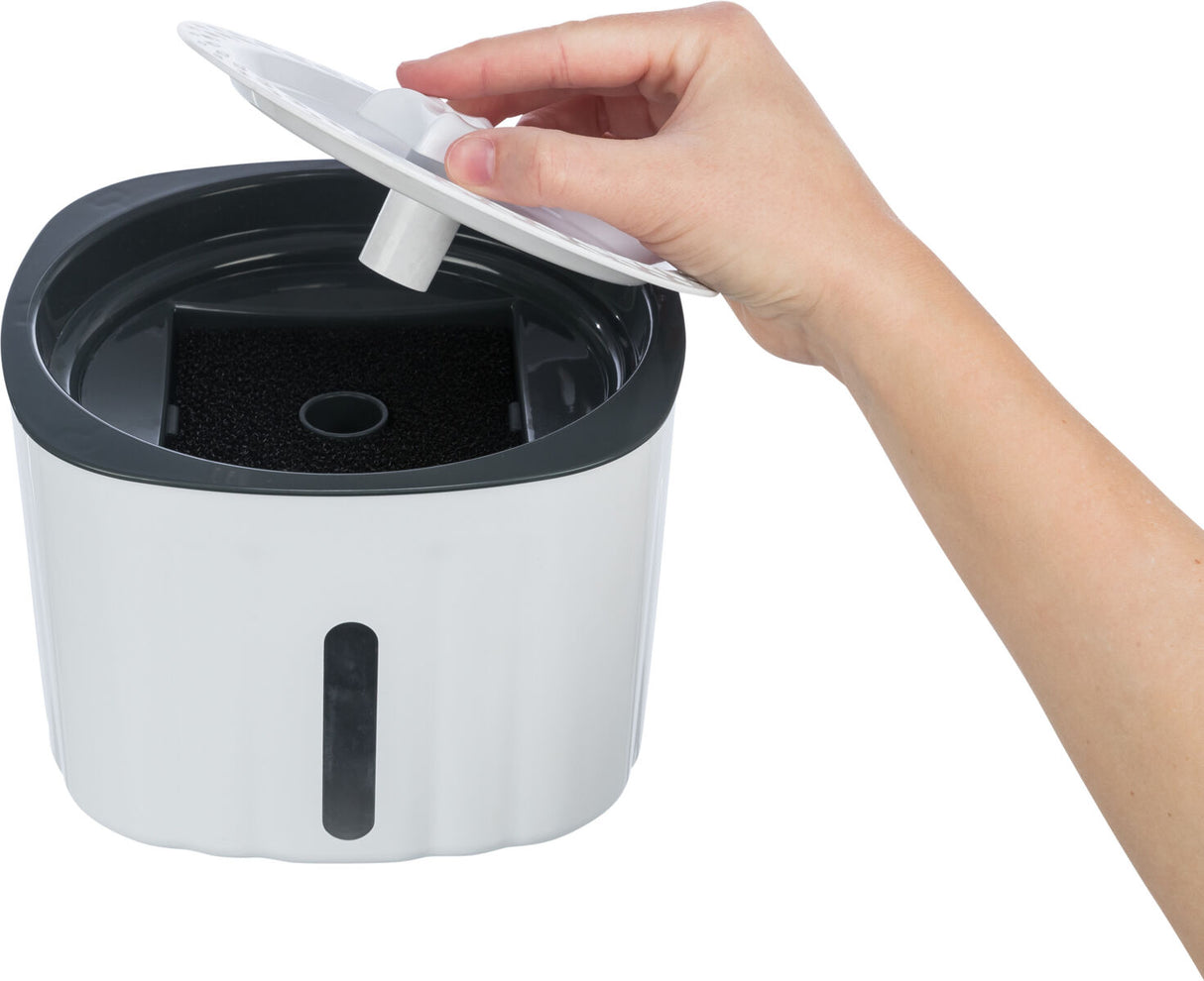 Eine Hand hebt den weißen Deckel eines weißen Behälters mit schwarzer Öffnung und Fenster an der Seite.