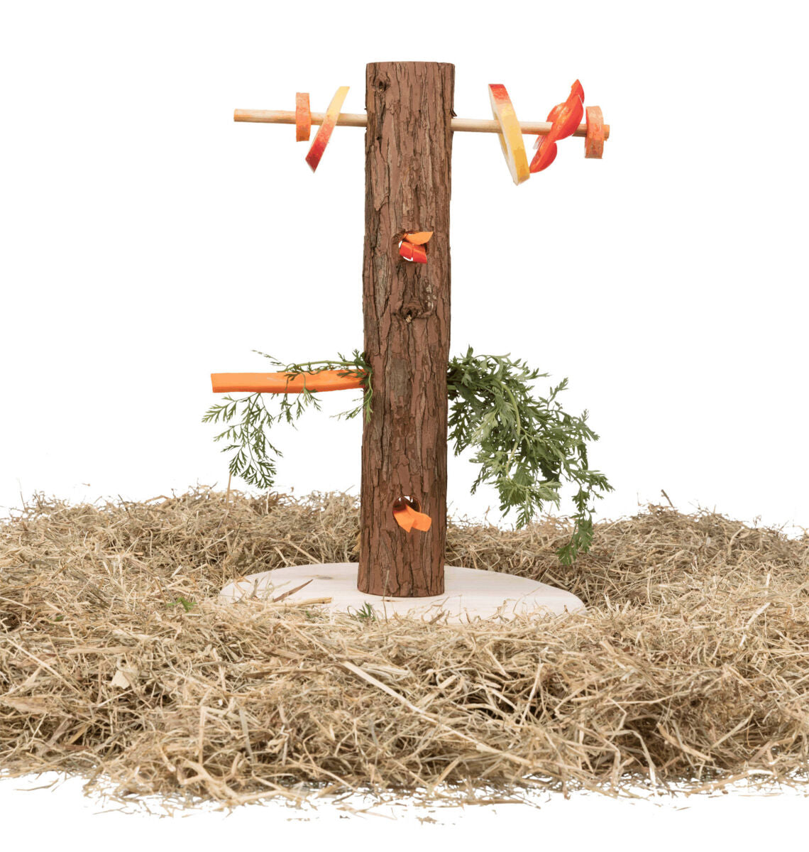 Holzpfosten mit Löchern und Zweigen, an dem orangefarbene und rote Gemüse- und Fruchtstücke angebracht sind, auf einer Basis aus Stroh.