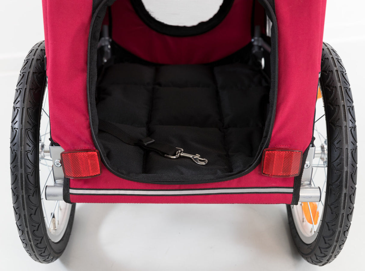 Roter Fahrradanhänger mit zwei schwarzen Rädern und einer schwarzen Innenpolsterung, erkennbar ist auch ein Haken.