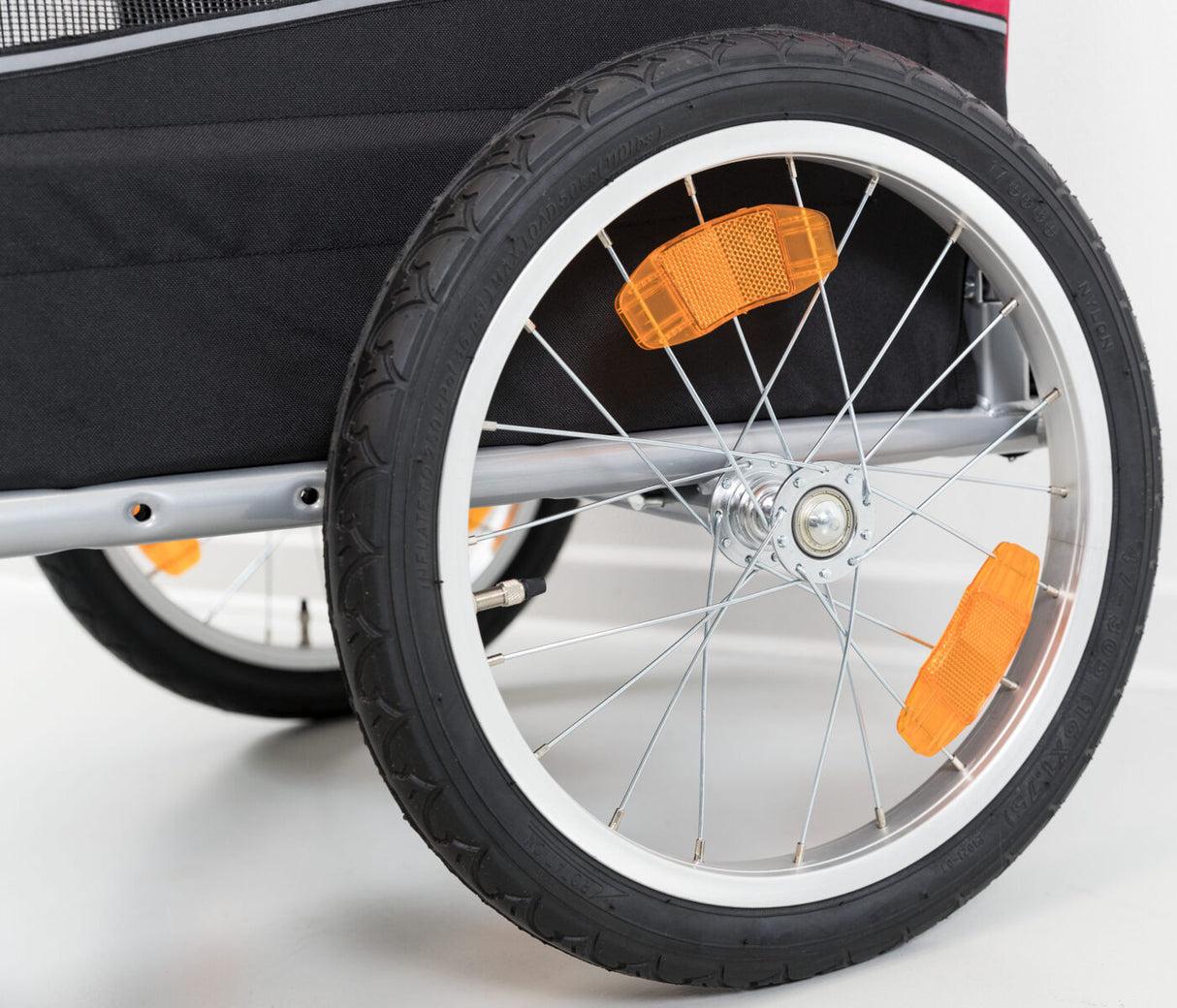 Rundes Rad eines schwarzen Fahrradanhängers mit silbernen Speichen und orangefarbenen Reflektoren.