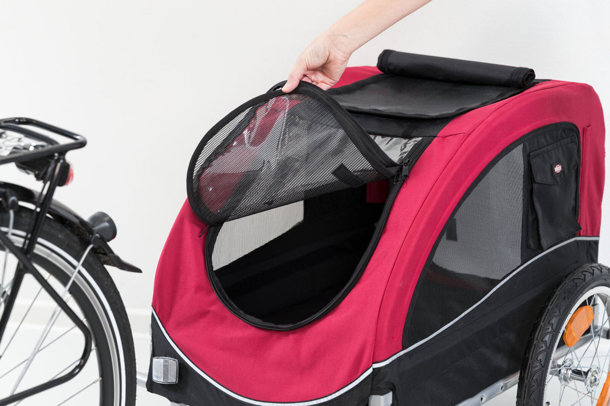 Ein roter Fahrradanhänger mit schwarzen Netzeinsätzen, ein Teil des Anhängers wird von einer Hand geöffnet.