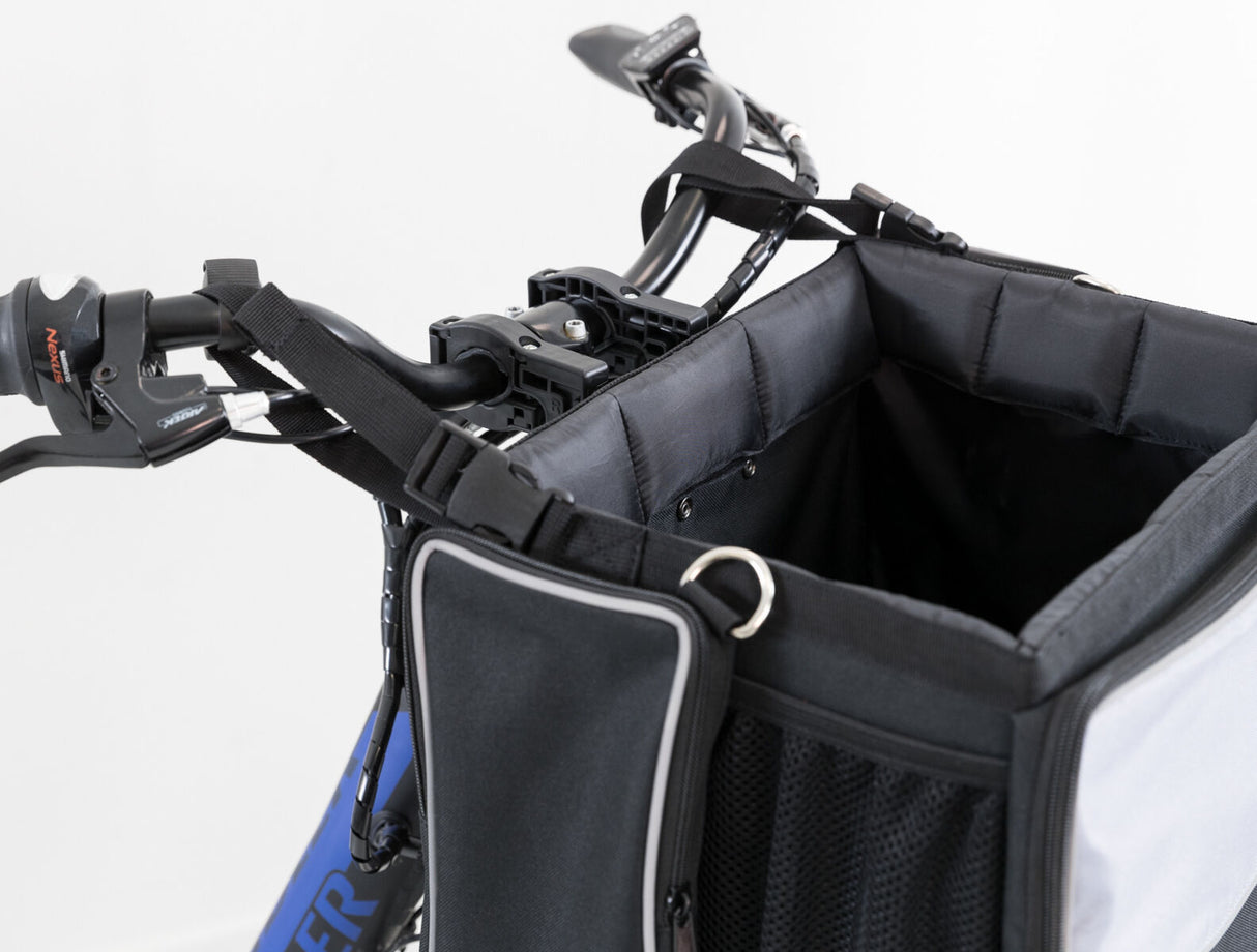 Schwarzer Fahrradkorb mit weichem Innenfutter, befestigt am Lenker mit Gurten, partiell sichtbarer blauer Rahmen.
