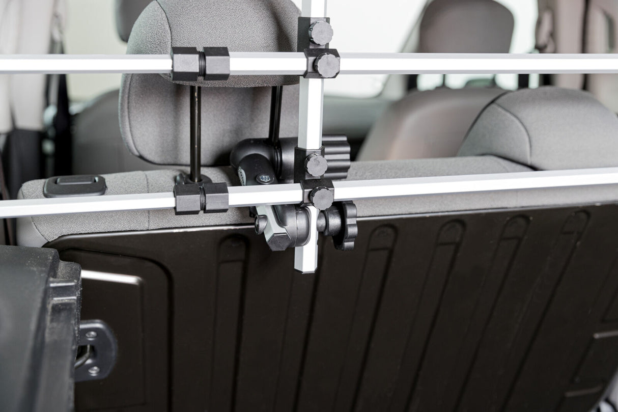 Eine silberne Kofferraum-Trennwand mit schwarzen Befestigungselementen, die an grauen Autositzen montiert ist.