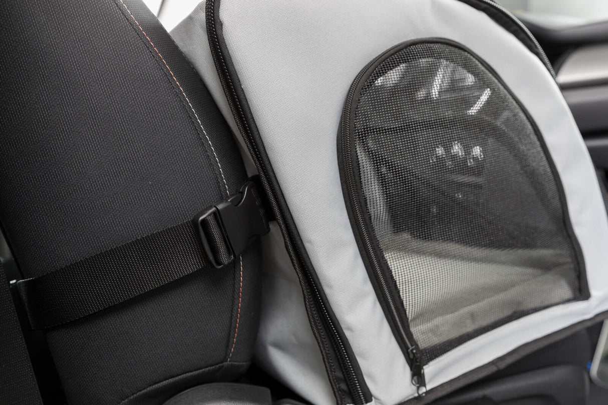 Grau-schwarzes Transportgerät im Auto, mit Netzfenster und Gurt an der Rückenlehne befestigt.