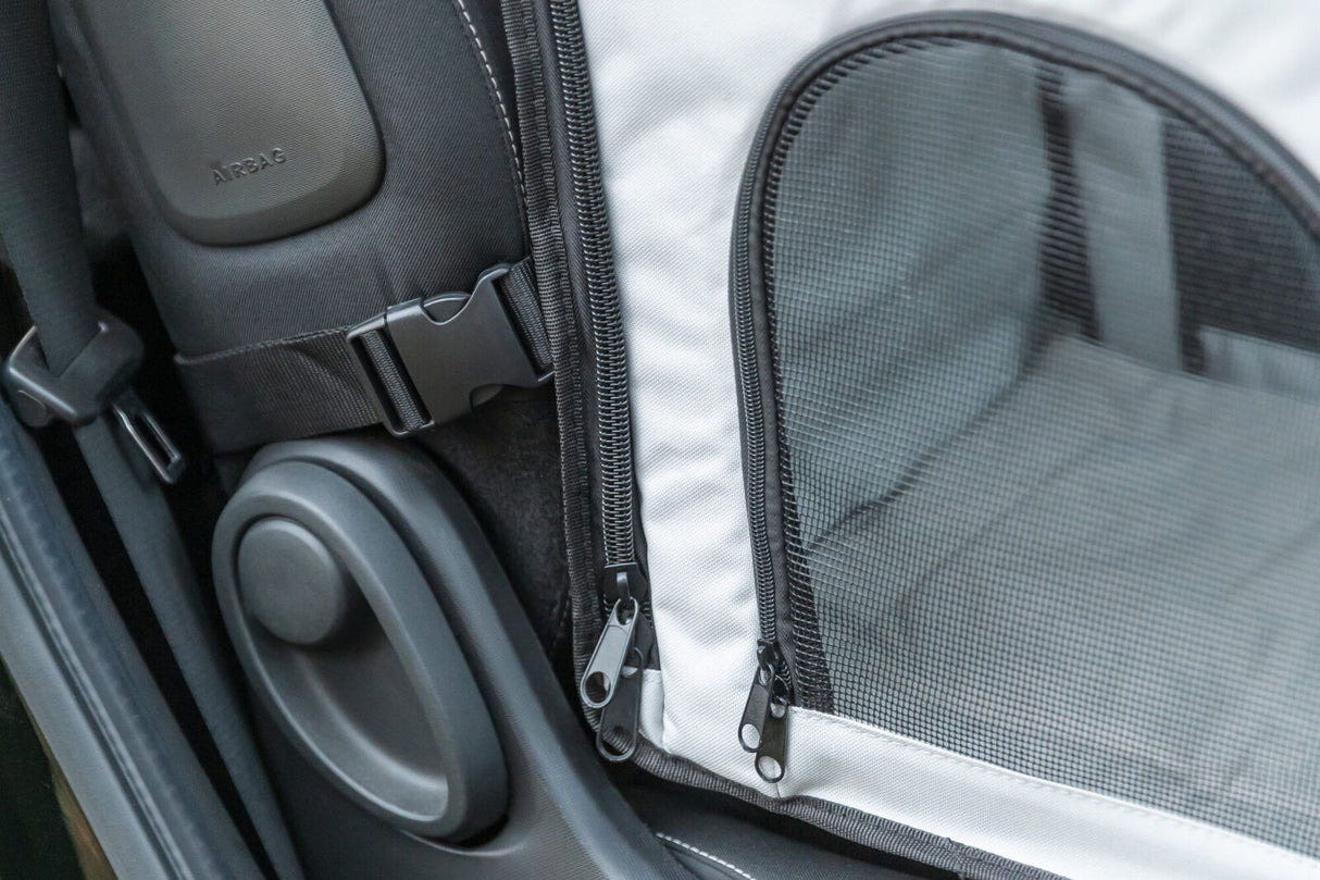 Nahaufnahme eines weißen Transportrucksacks mit schwarzem Netz und Reißverschlüssen im Auto.