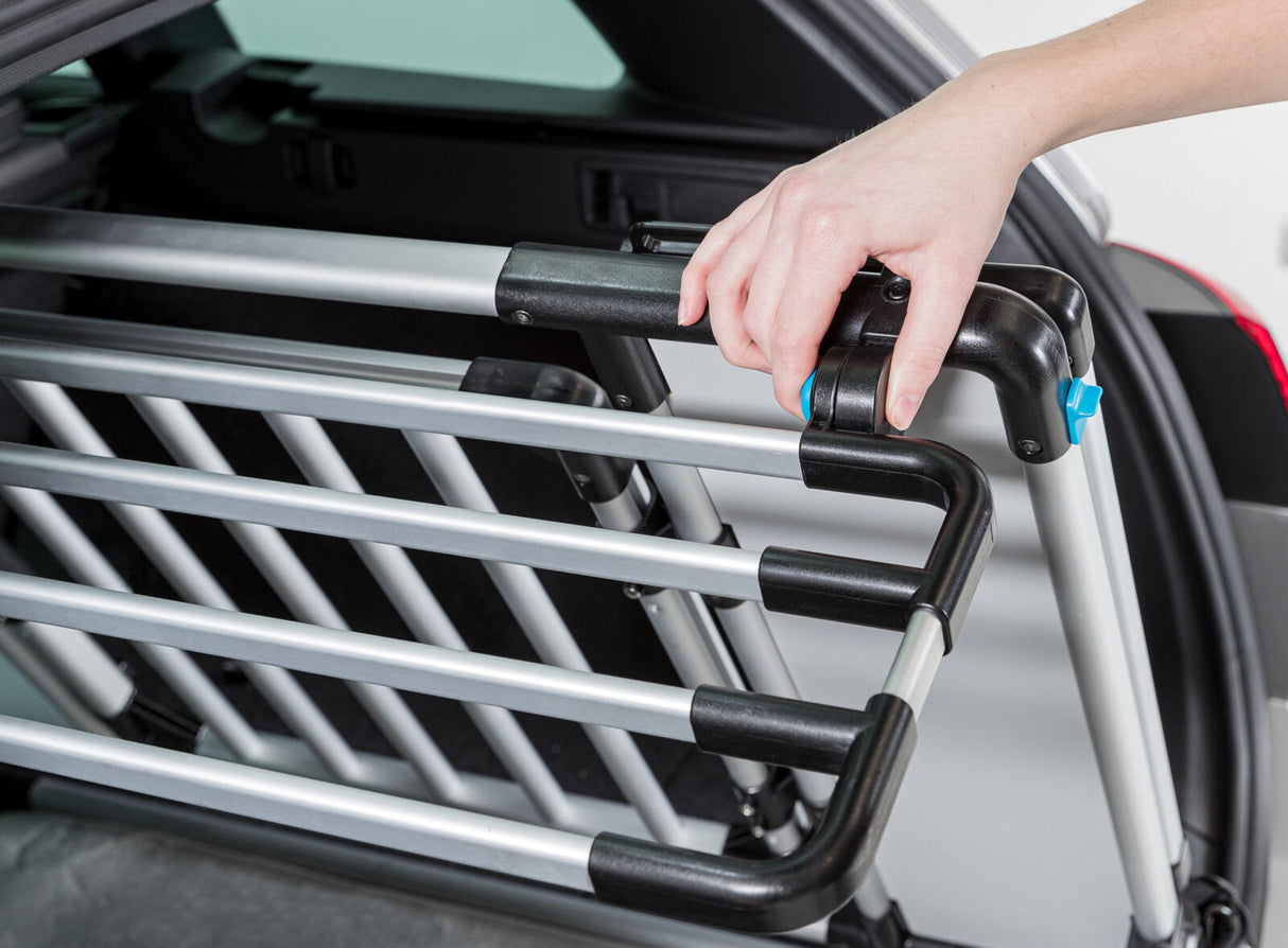 Eine Hand justiert ein silbernes Gitter mit schwarzen Elementen im Kofferraum eines Autos.