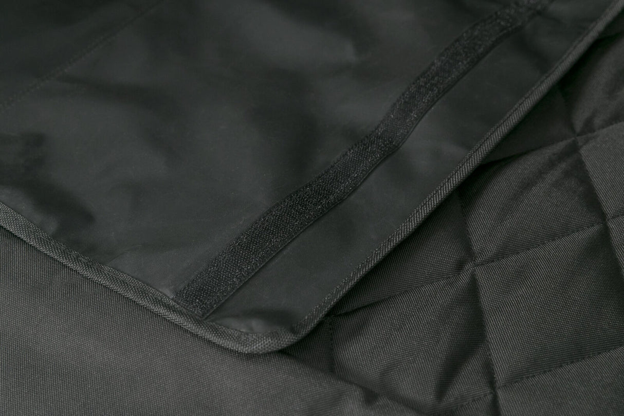 Schwarzes gewebtes Material mit diagonal verlaufender Naht und Klettverschluss auf einer Oberfläche.