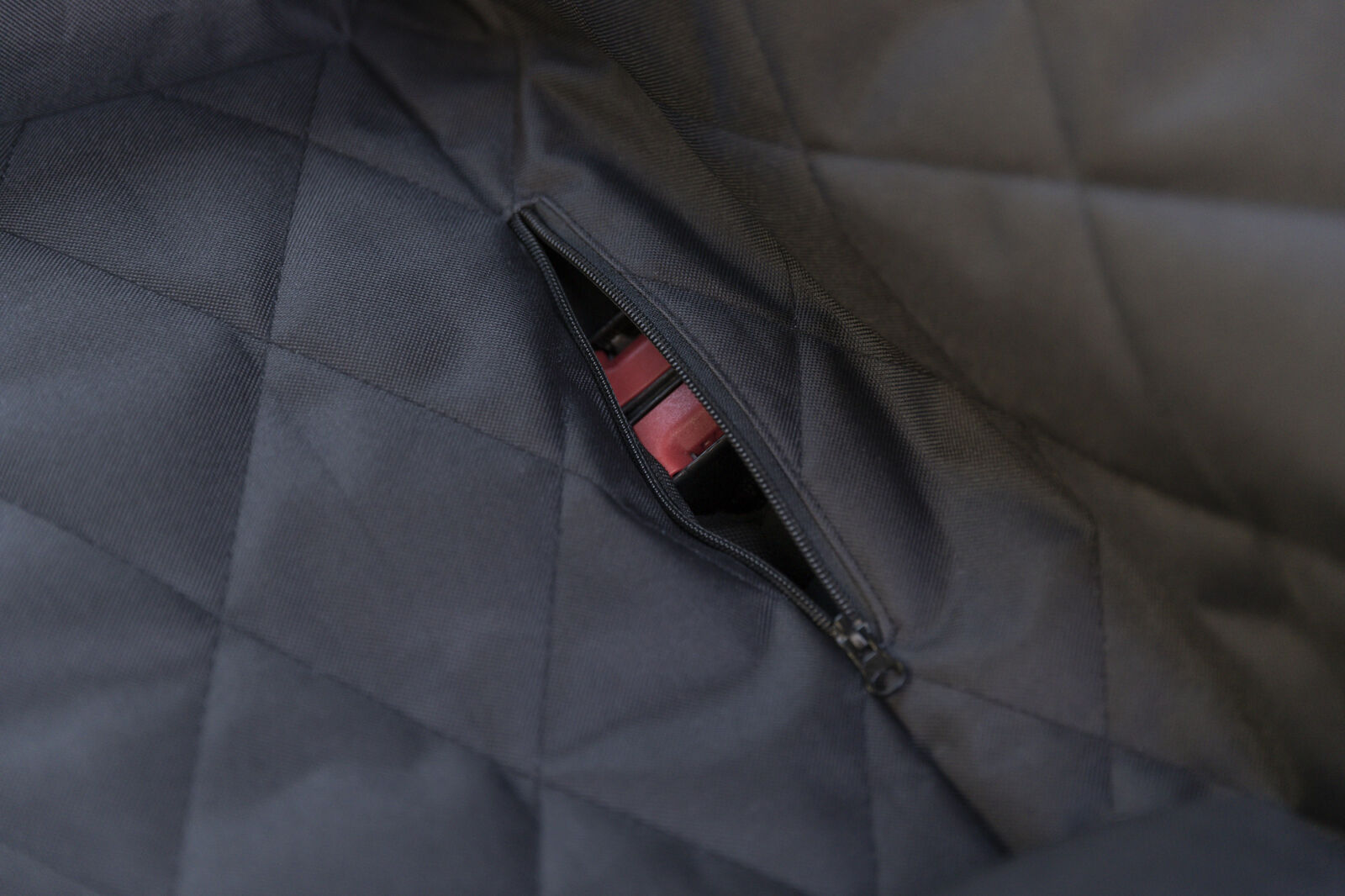 Ein schwarzer gepolsterter Stoff mit einem leicht geöffneten Reißverschluss, der rote Gegenstände zeigt.