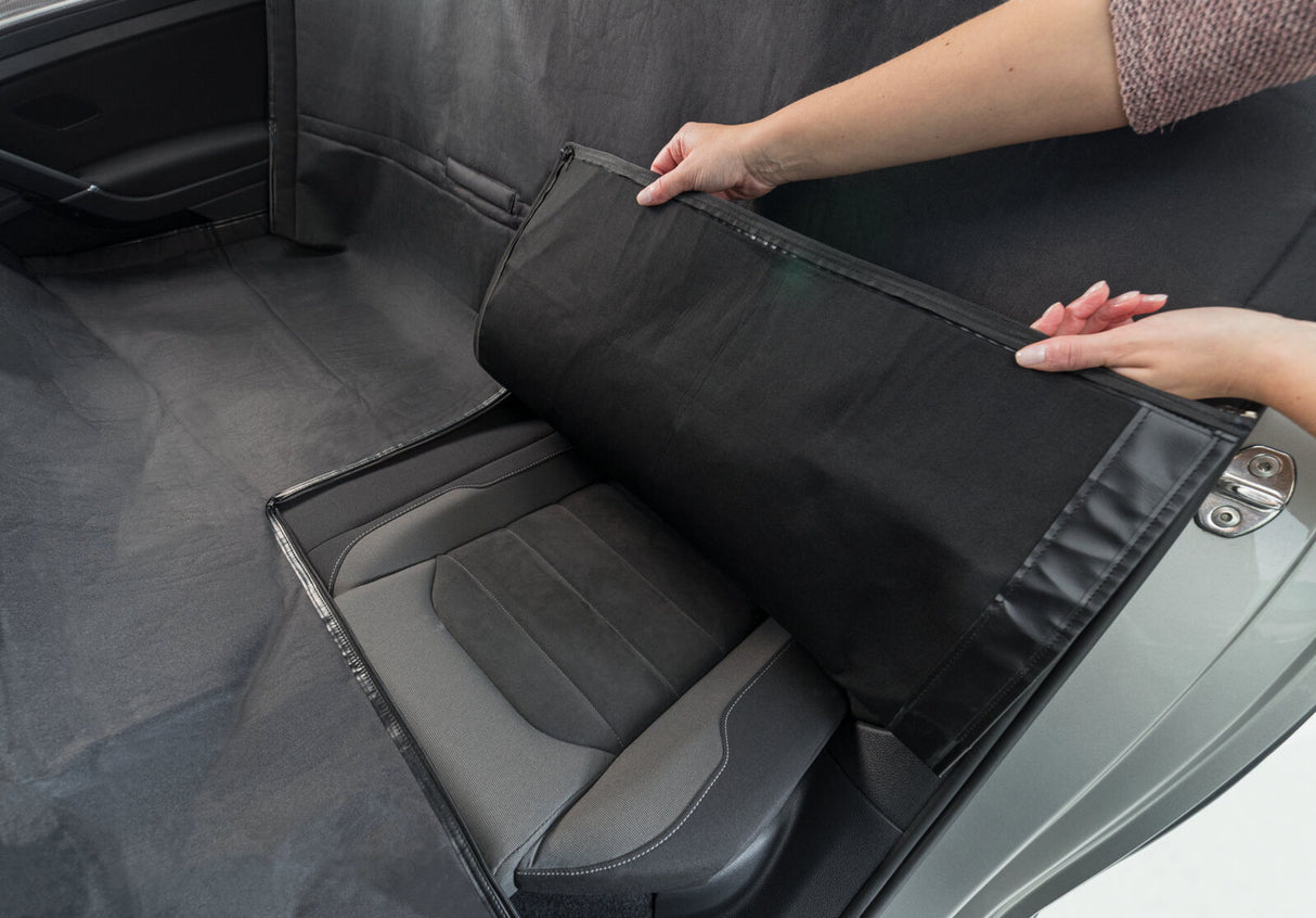 Ein Auto mit geöffneter Tür zeigt eine schwarze Sitzabdeckung, die von einer Person angehoben wird.