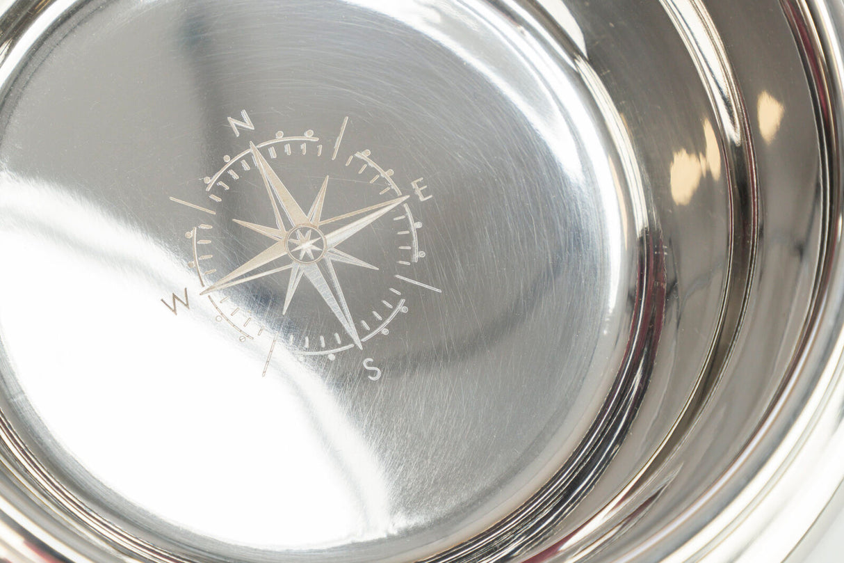 Eine glänzende silberne Metallschale mit einer gravierten Kompassrose im Inneren, die Himmelsrichtungen anzeigt.