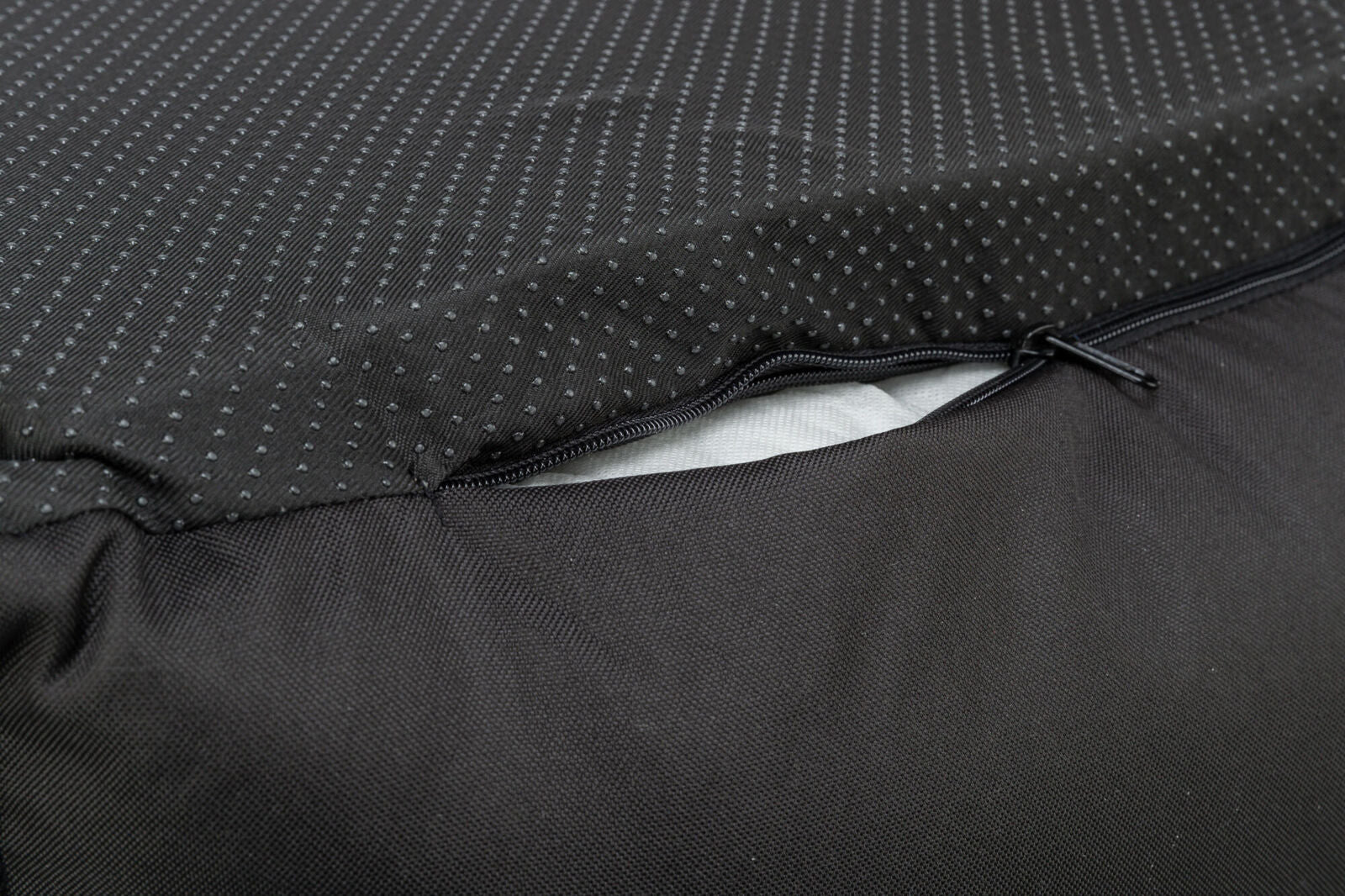 Nahaufnahme eines schwarzen Stoffes mit Punktmuster, ein Reißverschluss ist teilweise geöffnet und darunter ist weißes Material sichtbar.