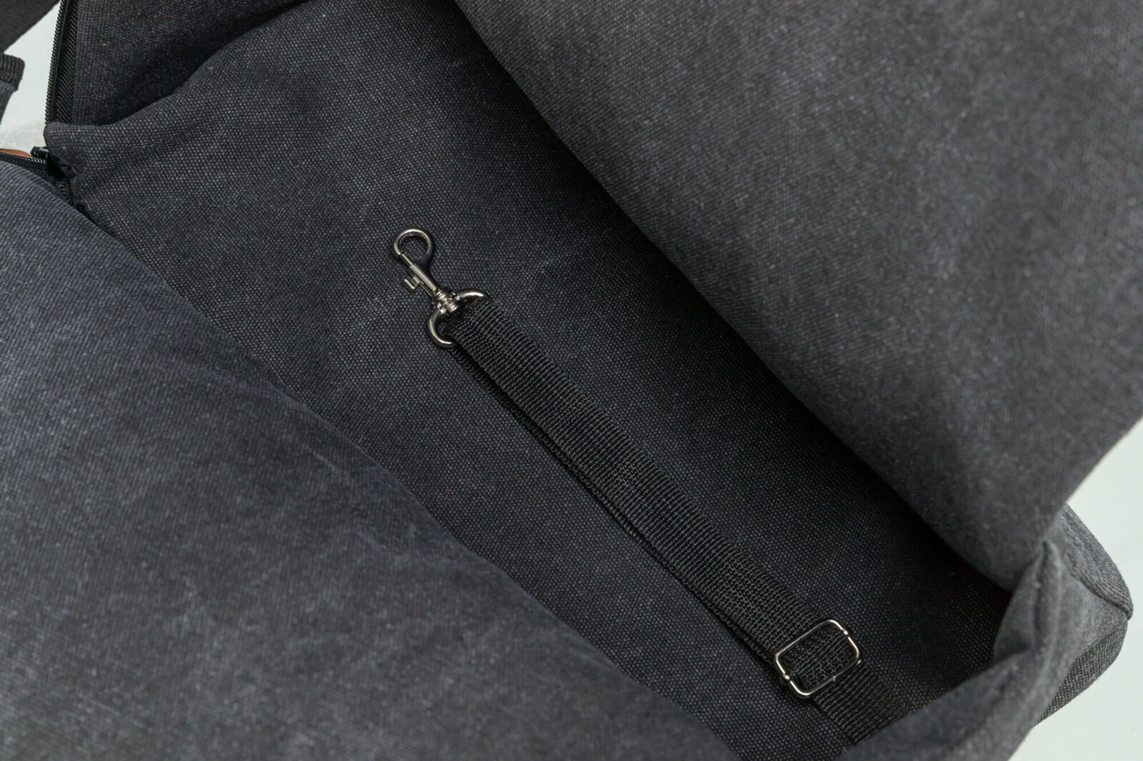 Innenbereich einer dunkelgrauen Tasche mit einem Nylongurt, der an einem kleinen Metallhaken befestigt ist.