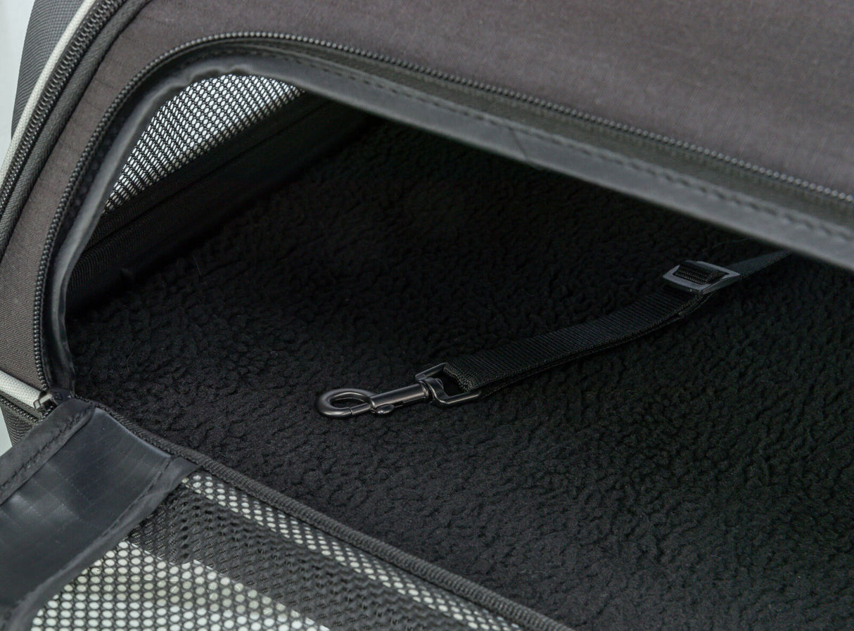 Schwarzes Innenfutter mit Riemen und Haken in einem geöffneten, teilweise schwarzen Tragebehälter mit Netzstoff.