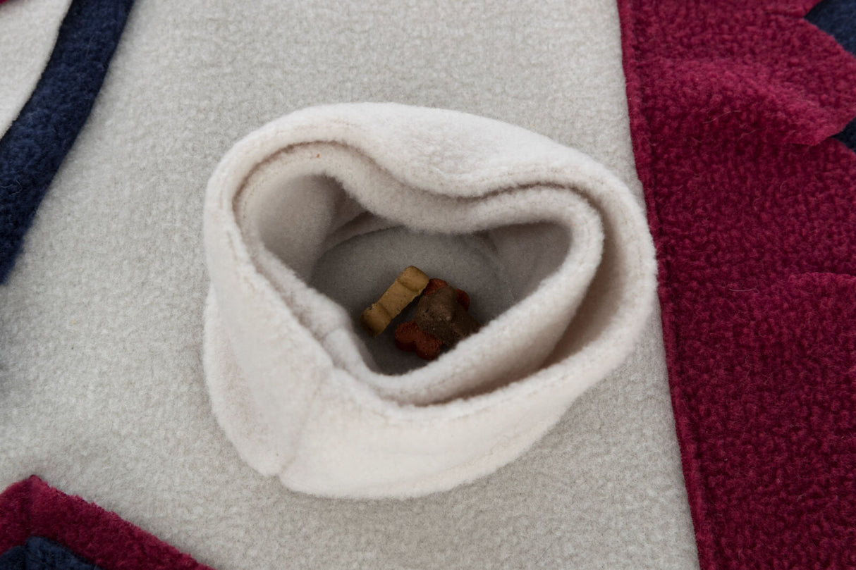 Beiger Stoff mit herzförmiger Öffnung, darin liegen kleine, bunte Kauknochen auf mehrfarbigem Hintergrund.