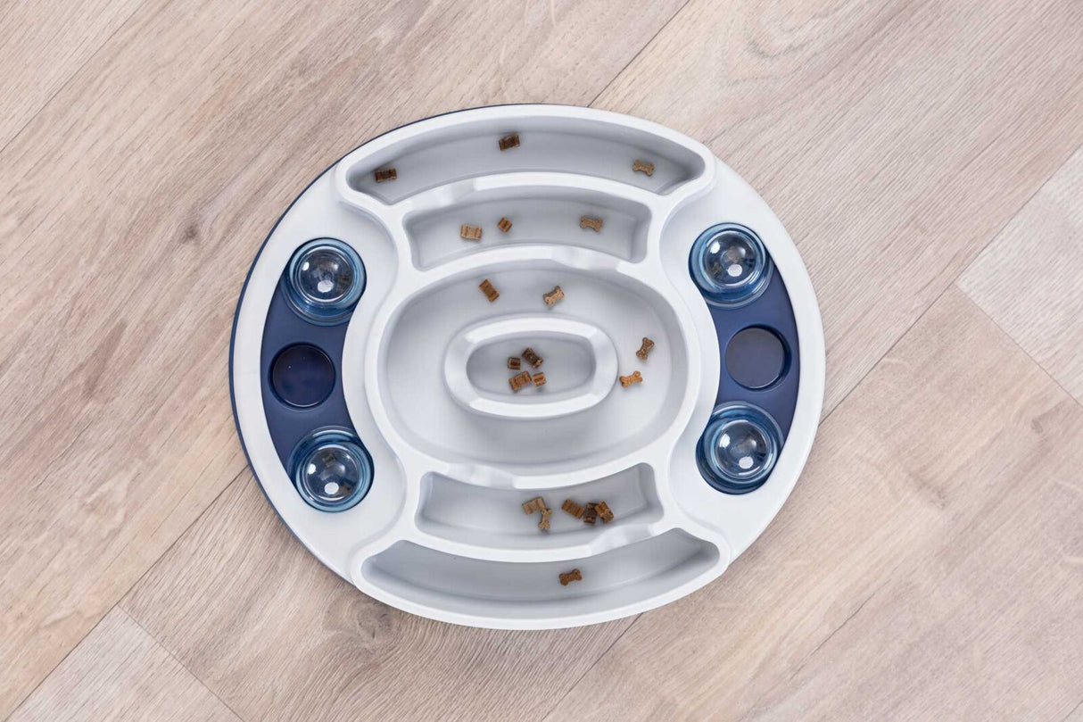 Rundes, weiß-blaues Geschicklichkeitsspiel mit vertieften Bahnen und transparenten Abdeckungen, gefüllt mit kleinen Leckerbissen.