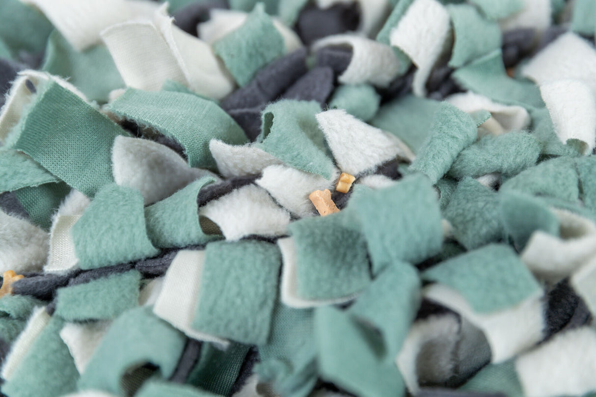 Verschiedene Stoffstreifen in Grün-, Weiß- und Grautönen sind verwoben, mit kleinen beigen Stücken darin.