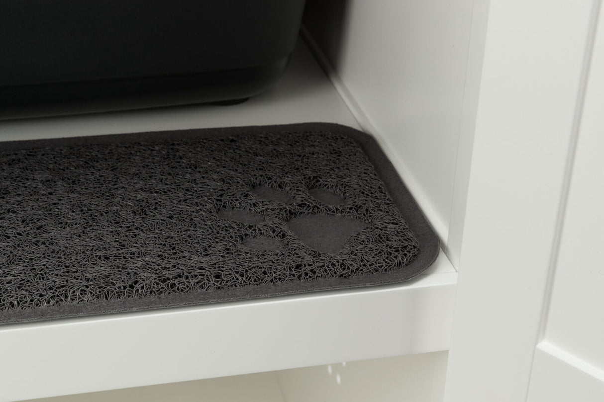 Dunkle Matte mit Pfotenabdruck-Muster auf einem weißen Regal neben einem schwarzen Behälter.