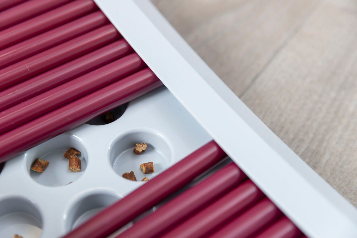 Weiße und rote strukturierte Kunststoffoberfläche mit kleinen braunen Stücken in Vertiefungen, auf hellem Hintergrund.