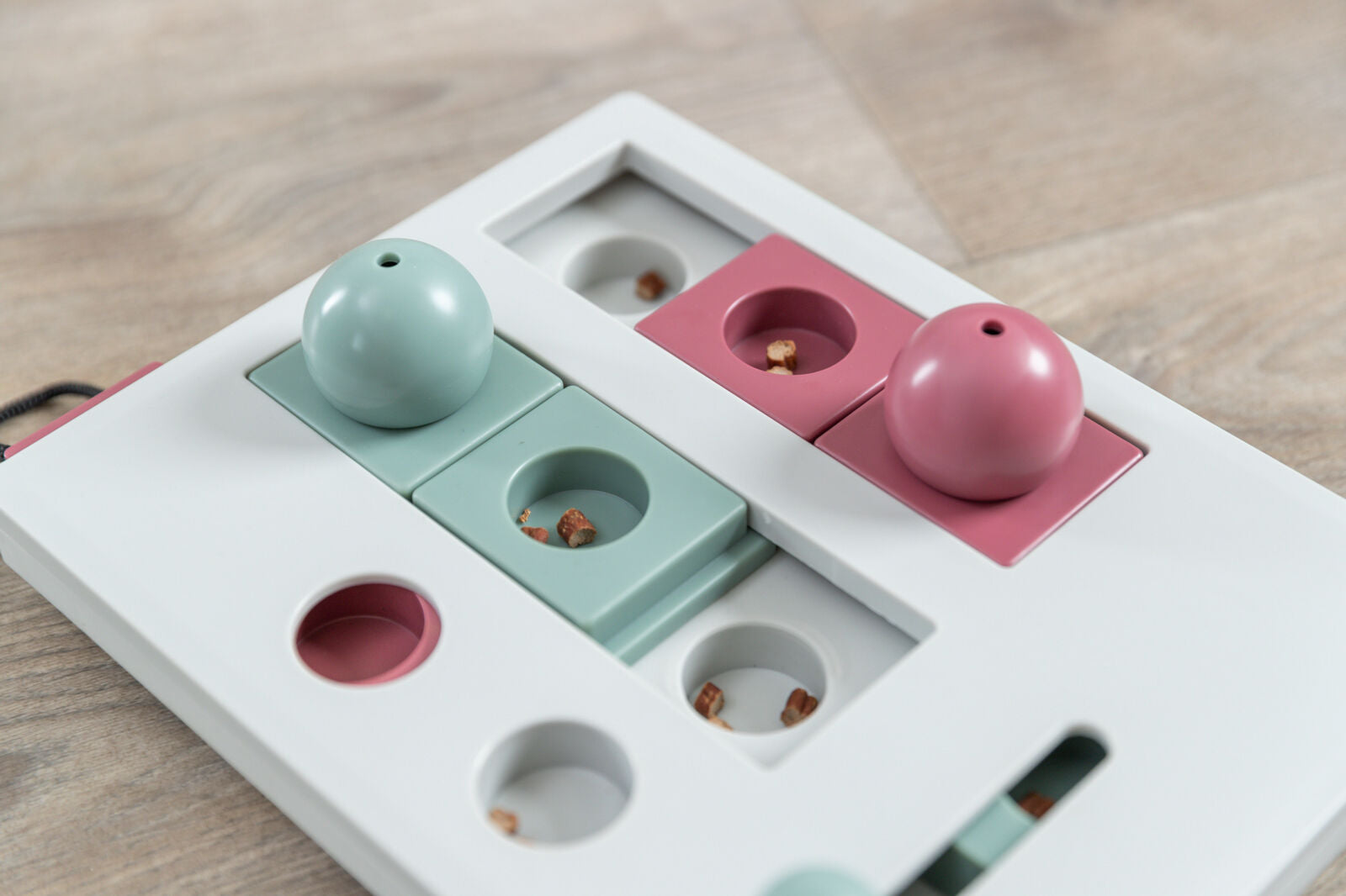 Weißes Spielzeug mit rosafarbenen und mintgrünen Bauteilen sowie runden Abdeckungen, darunter kleine Leckerlis.