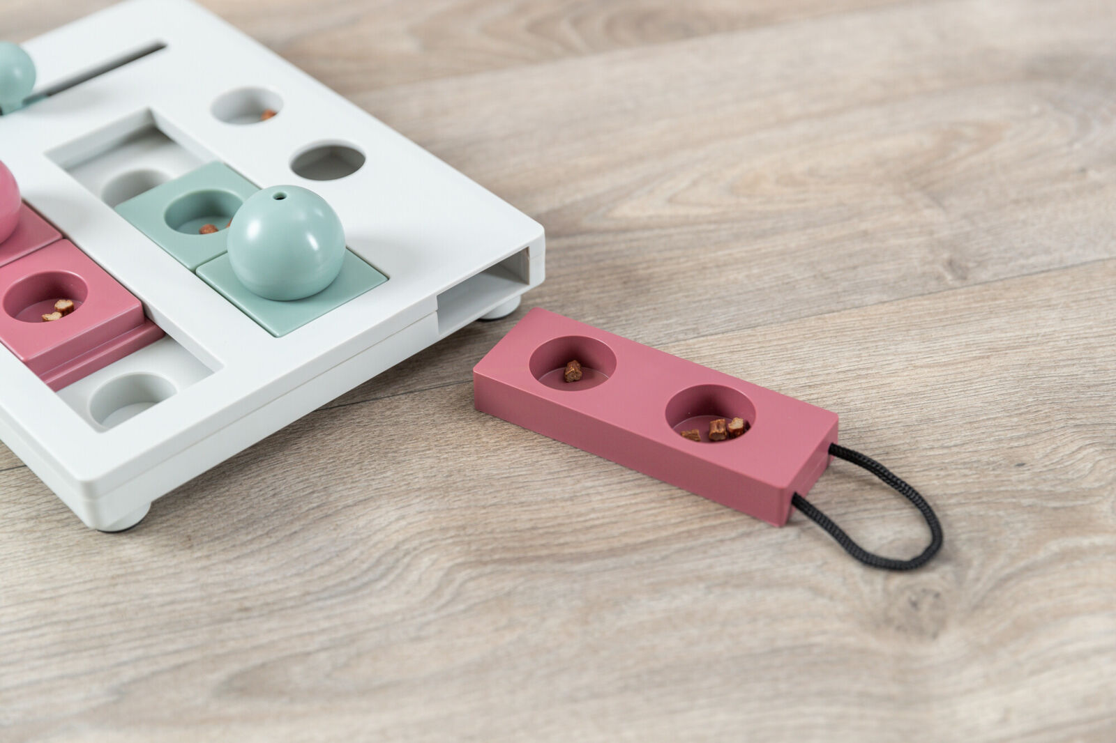 Puzzle-Spielzeug mit rot-weißen Elementen und Snacks in Mulden auf Holzfußboden.