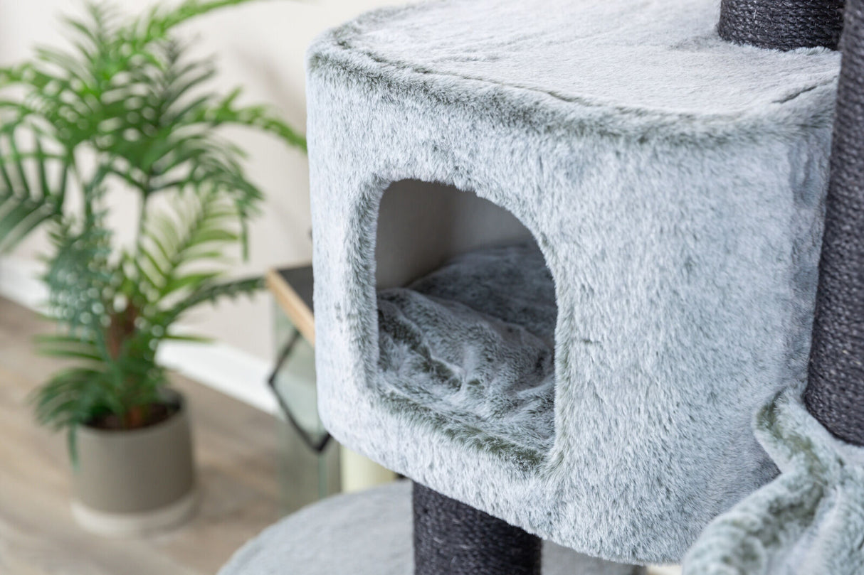 Graues, flauschiges Möbelstück mit einer Höhle, im Hintergrund ist ein grüner Zimmerpflanze.