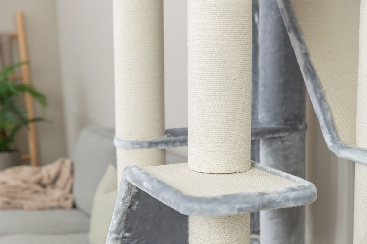 Kratzturm aus hellem Stoff mit grauen Plüscheinfassungen vor Sofa im Wohnzimmer.