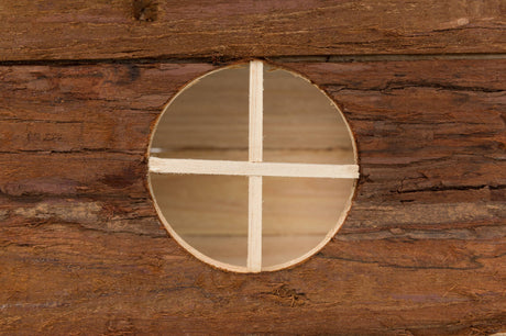 Runde Öffnung in einer Holzwand mit einem Kreuz aus dünnen Holzlatten in der Mitte.