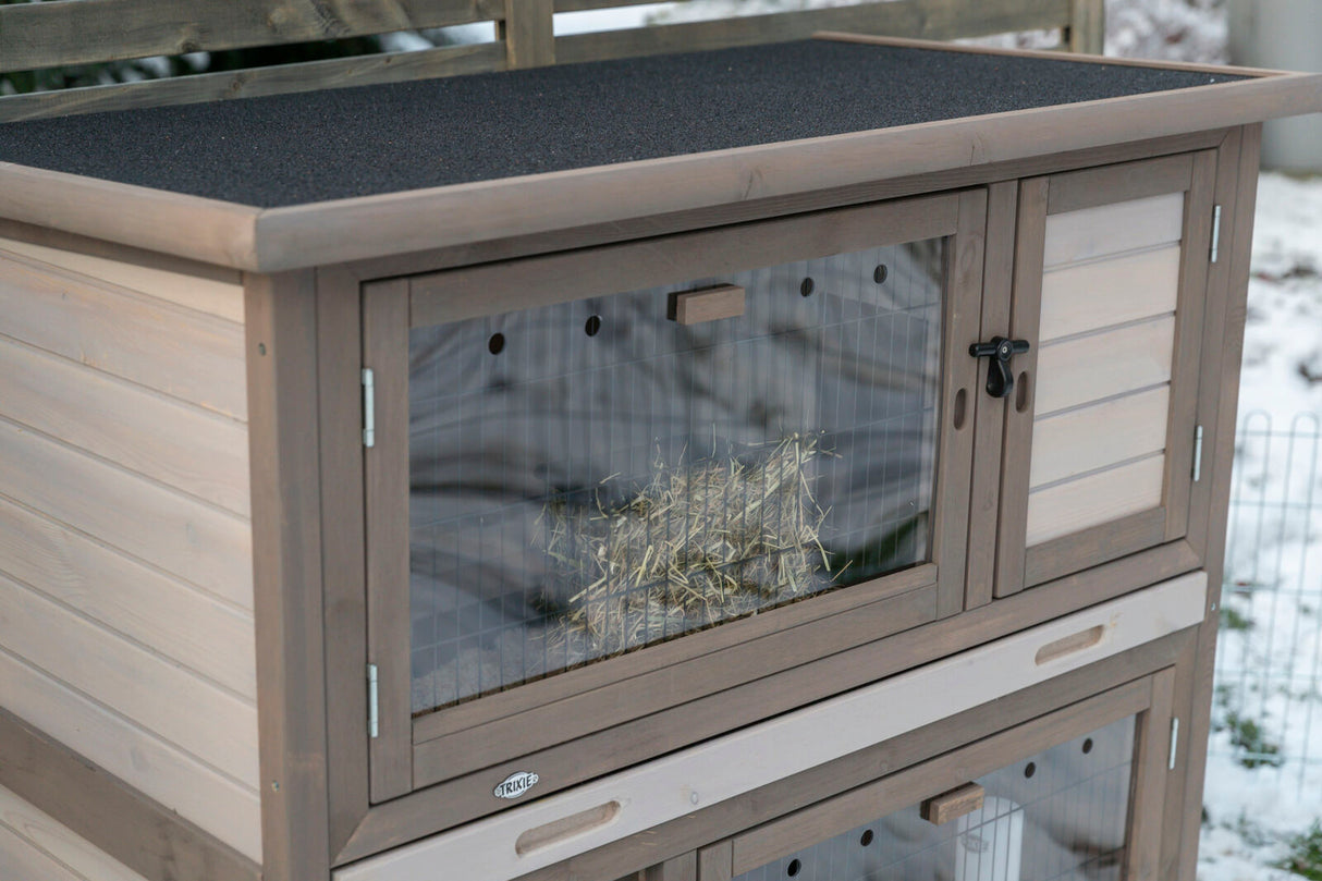 Holzkaninchenstall mit zwei Etagen, transparenten Kunststofftüren und einem Dach aus schwarzem Material, innen Heu sichtbar.