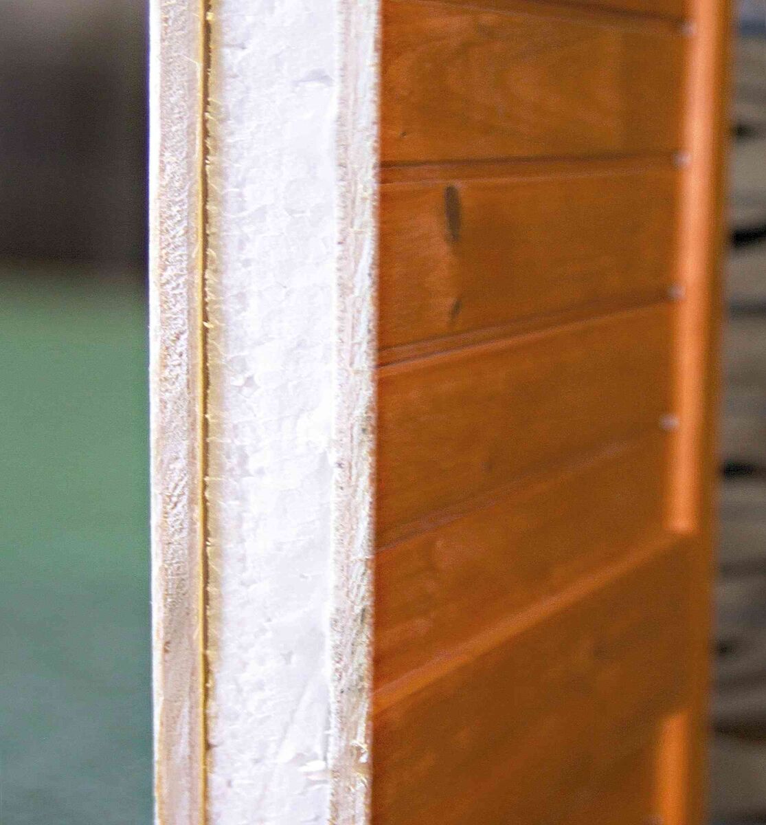 Holztür mit seitlicher Kantenansicht, zeigt helles Isoliermaterial und vertikale Holzpaneele in Braun.